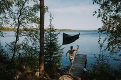 Alaston mies juoksee laituria pitkin järveen, tumma pyyhe on heitetty ilmaan.