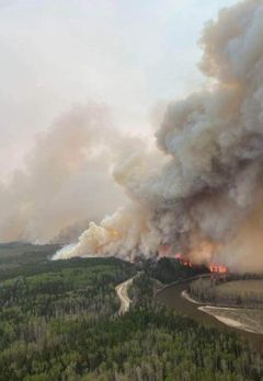 Ilmakuva metsäpalosta. Savua nousee koko taivaan peittävästi laajalta alueelta silmän kantamattomiin jatkuvassa metsässä. Kuvan etualalta johtaa tie keskelle paloaluetta.