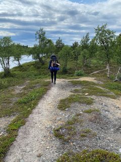 Vaeltaja kävelee rinkka selässä polkua pitkin joen varrella.