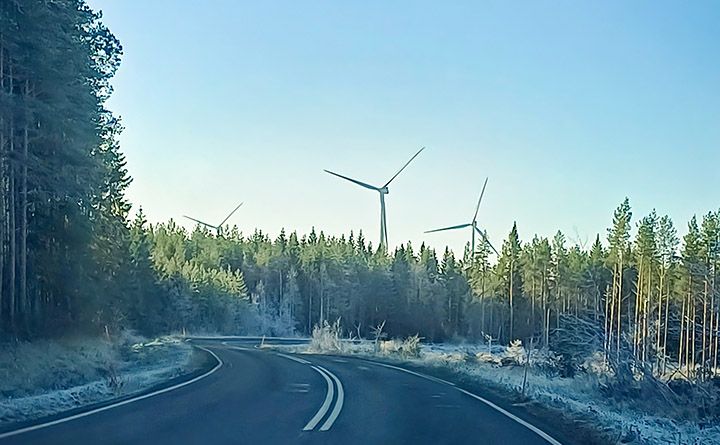 Metsän halki kulkeva maantie, metsän takana tuulivoimaloita.