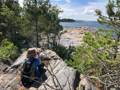 Lapsi istuu kalliolla selkä kameraan päin ja kiikaroi merelle.