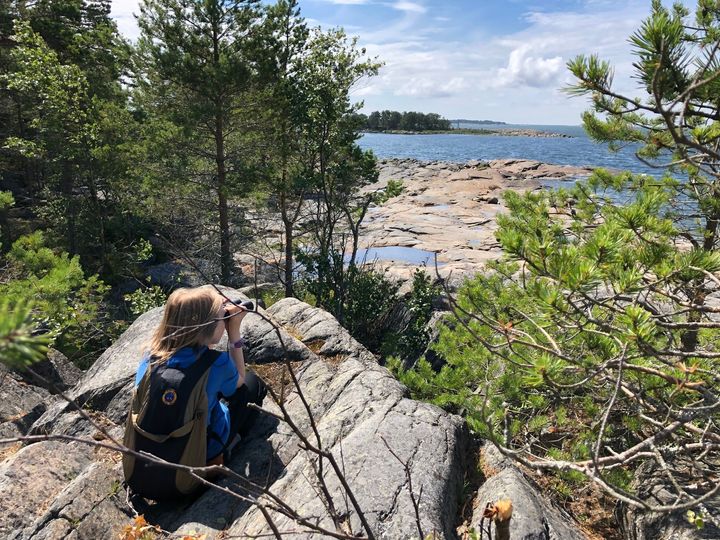 Barnet sitter på en klippa och tittar ut i kikaren på havet