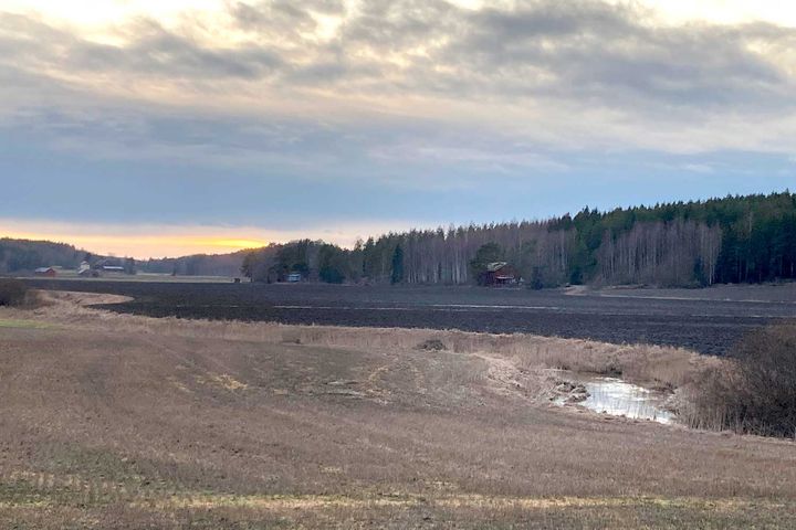 Peltomaisema joen varrella, joen takana kynnettyä peltoa ja punainen lato.