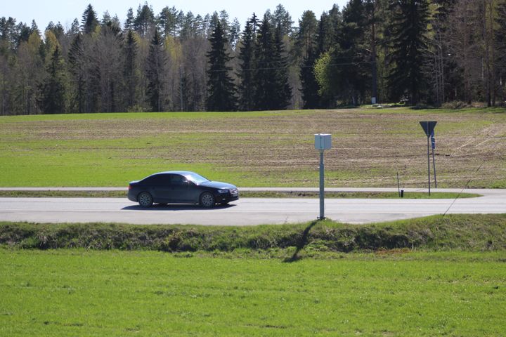 Auto lähestyy nopeusvalvontakameraa alkukeväisellä maantiellä.