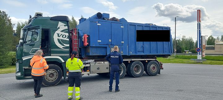 Kolme viranomaista tarkastaa jätekuljetusrekkaa pysäköintialueella.