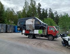 Rekan lavalle on kuormattu pakettiauto. Taustalla näkyy puita ja roskasäiliöitä.