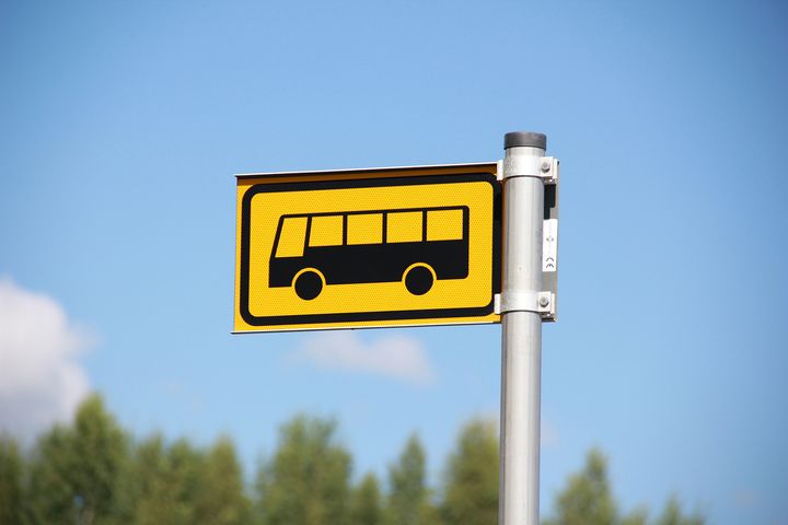 Linja-autopysäkin liikennemerkki, taustalla sinitaivas ja metsää.