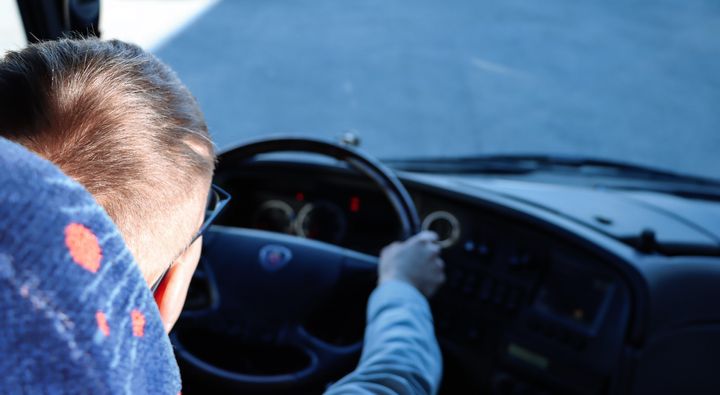 Henkilö ajaa linja-autoa, katsoen eteenpäin kohti tietä.