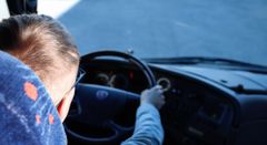 Henkilö ajaa linja-autoa, katsoen eteenpäin kohti tietä.