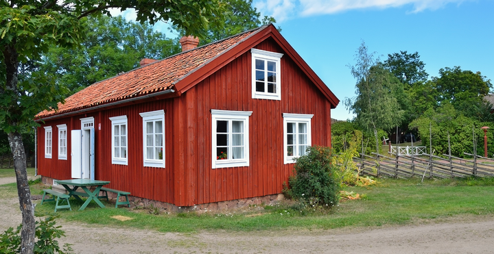 Kuvassa tyypillinen punainen mökki, suomalaisessa maalaismaisemassa