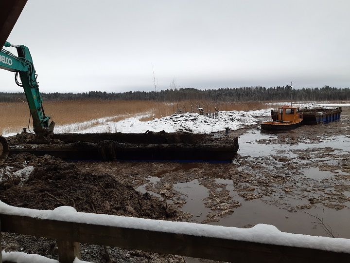 Lintuvedellä proomu ruoppaamassa rannassa.