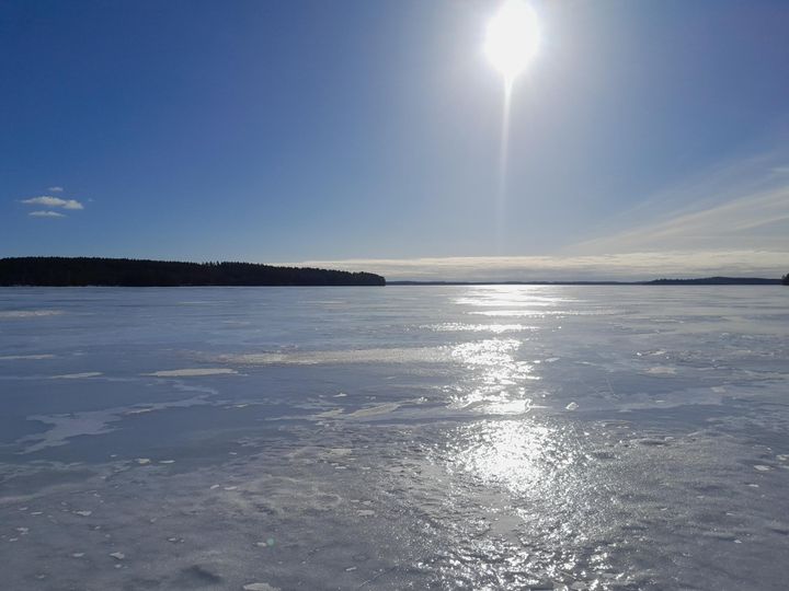 Aurinko paistaa lumettomalle jäälle Korpijärvellä, muodostaen siltamaisen heijastuman röpelömäisen jään pintaan.