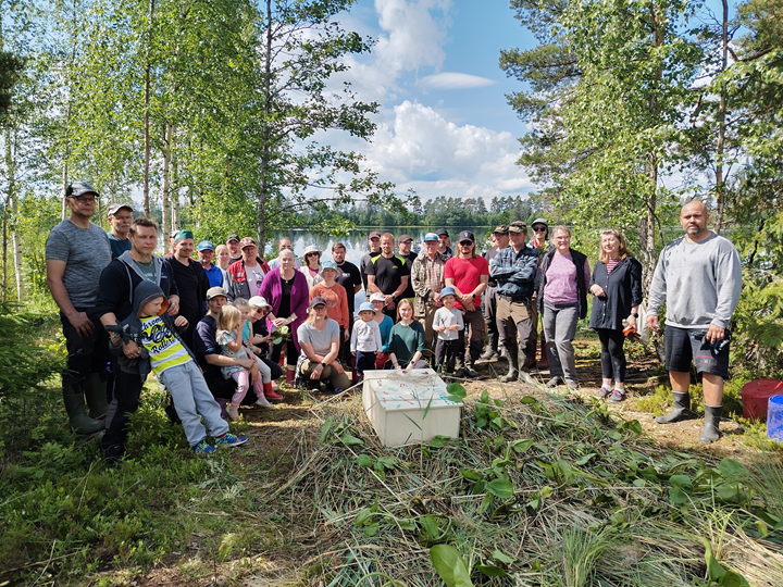 Ryhmä ihmisiä kesällä järven rannalla rakentamassa kosteikkolauttoja.