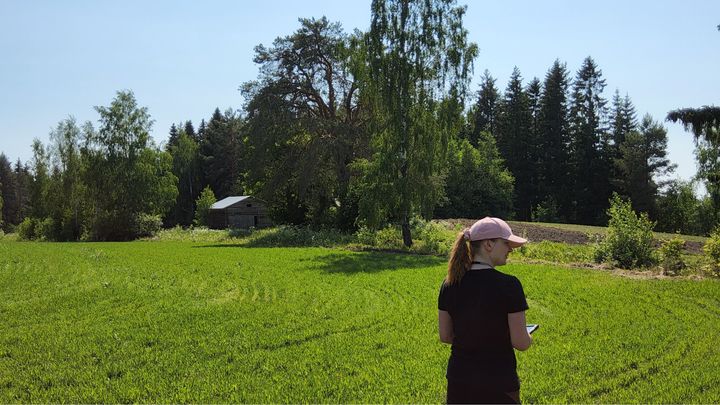 Ihminen pellolla, taustalla puita ja lato