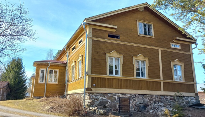 Ahvenniemen tilan päärakennus, vanhanaikainen puurakennus, jossa on kaksi kerrosta ja porstua, kuvattu  alhaalta päin sinistä  taivasta vasten