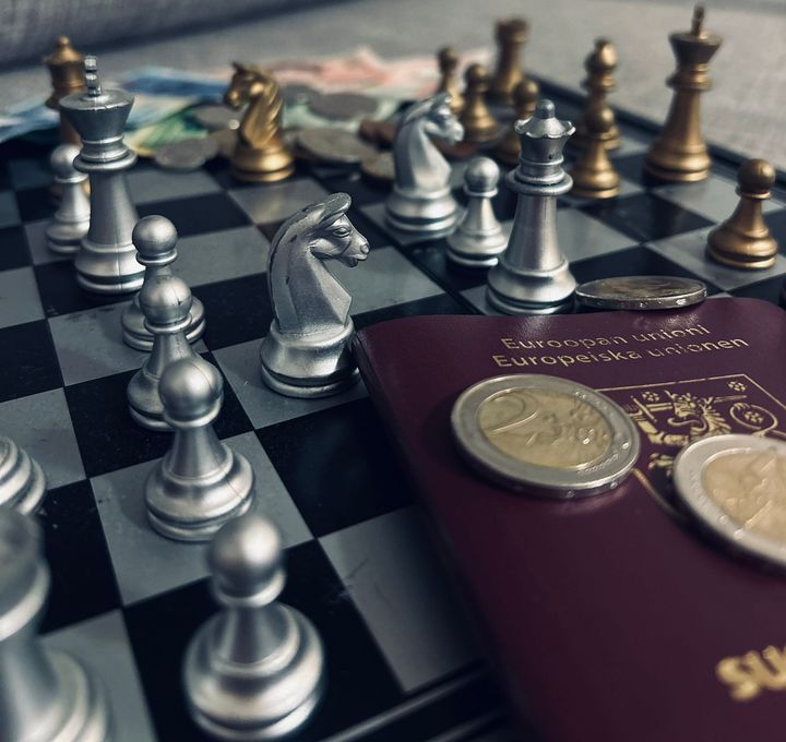 Kuvituskuva, jossa shakkilaudalle on aseteltu shakkinappuloiden lisäksi passi ja käteistä