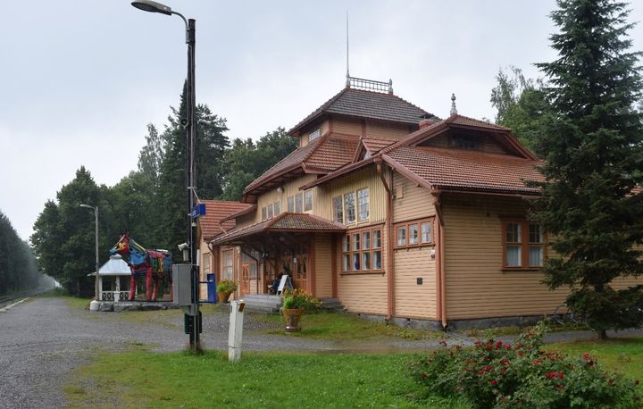 Luston asemarakennus, joka on vanha puurakennus ja vieressä asemapuistoa. Lehmuskuja kulkee radan vieressä vasemmalla.