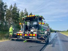 Asfalttikone päällystää tietä metsän vieressä, työntekijä tarkistaa asiakirjoja.