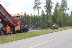 Työmiehet työskentelevät asfaltinlevityskoneen ja jyrän kanssa tien päällystystöissä.