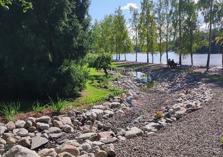 Kivinen hulevesijärjestelmä puiden ympäröimänä, taustalla järvimaisema.