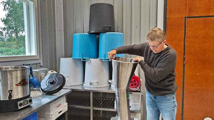 Kuvassa näkyy yksi henkilö, muovisia saaveja ja mehustamon laitteita.