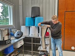 Kuvassa mehustamossa yksi henkilö, mehustamon laitteita ja muovisia saaveja.