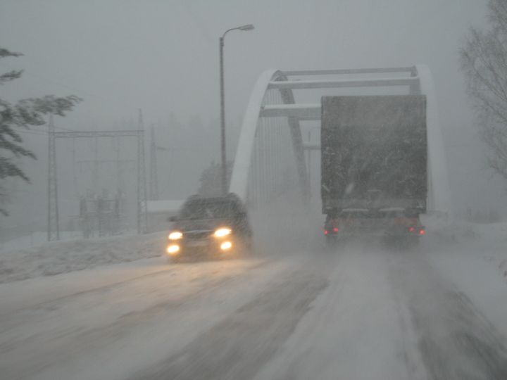 Auto ja rekka ohittavat toisensa huonossa ajokelissä talvella, ja taustalla näkyy sillan pylväät.