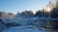 Kuohuva koskimaisema, aurinko puiden takana, lunta maassa ja huurteisia puita.