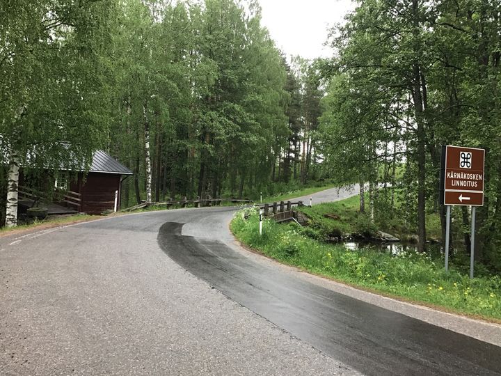 Asvalttitie kaartaa kivisillalle, jonka lähellä on liikennemerkki Kärnäkosken linnakkeesta.