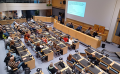 Ihmisiä istuu kaupungintalon kokoushuoneessa seuraten liikenneturvallisuusfoorumin esitystä.