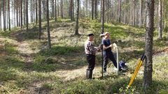 Kaksi henkilöä mittaamassa pohjaveden pintaa metsikössä.