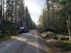 Metsäinen hiekkatie, jonka vieressä metsäkone työskentelee.
