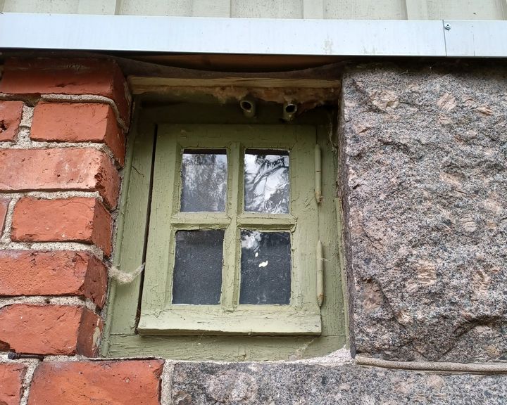 Vanha pieni ikkuna, jonka ympärillä tiiliseinää ja kiveä.