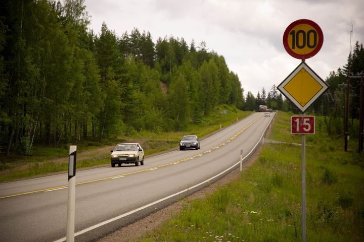 Kaksi autoa ajaa maalaismaisemassa mutkaisella maantiellä, nopeusrajoitus on 100 km/h.