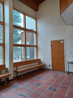 Tehtaanmäen koulun aulatila, jossa on puupenkit, laattalattiaa ja suuret ikkunat.