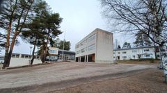 Kuva koulurakennuksesta, jota ympäröivät puut ja piha.