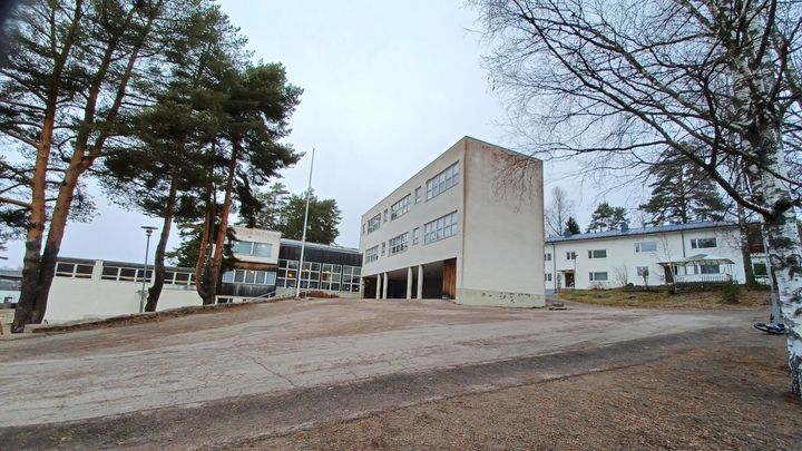 Kuva koulurakennuksesta, jota ympäröivät puut ja piha.