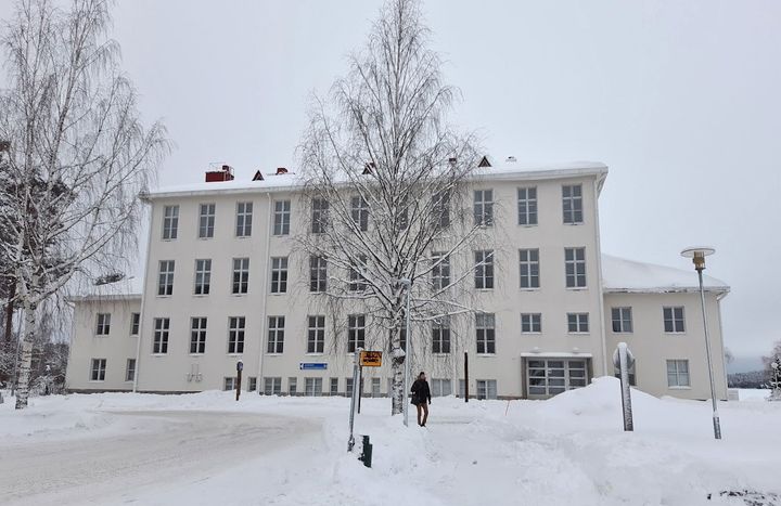 Talvinen kuva kolmikerroksisesta vaaleasta rakennuksesta.