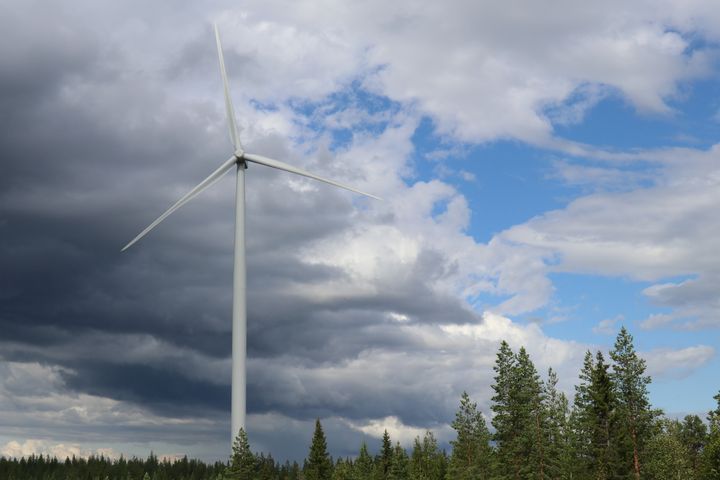 Tuulimylly maisemassa, puolipilvinen kesätaivas ja taustalla metsänreunassa puita.