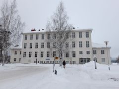 Valkoinen, kivinen koulurakennus, jossa paljon ikkunoita. Talvinen maisema.