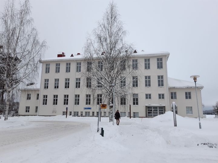 Valkoinen, kivinen koulurakennus, jossa paljon ikkunoita. Talvinen maisema.