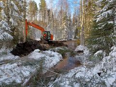 Kaivinkone kaivaa ojaa metsään, josta pieni kaistale on raivattu allasta varten. Maassa on hieman lunta.