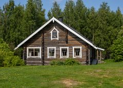 Hirsitalo koristeellisilla laudoilla, taustalla metsää.