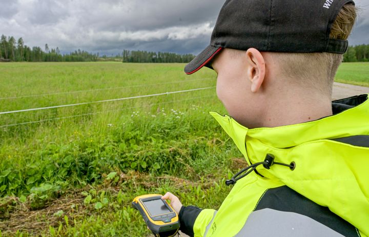 Huomioliiviin pukeutunut henkilö pellon laidalla gps-paikannin kädessään.