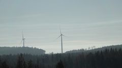 Kaksi tuulivoimalaa metsäisessä maisemassa.
