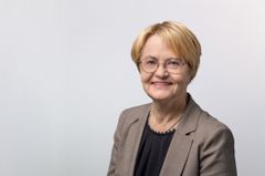 Nainen seisoo hymyillen harmaassa bleiserissä.