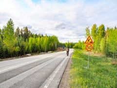 Pyöräilijä polkemassa kamerasta pois päin maantiellä. Tien vieressä kyltti tietyömaasta sekä 50 km/h nopeusrajoitus. Tien toisella puolella työmaa, jossa tehdään kevyen liikenteen väylää.