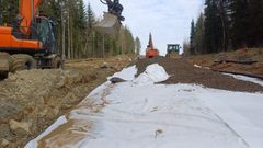 Rakennustyömaa metsän keskellä, jossa näkyy kaivinkone ja maansiirtoauto. Polulle levitetty valkoinen suojakangas ja soraa.
