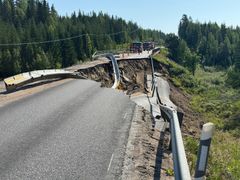 Tienosuus on romahtanut ja sortunut reunalta, jättäen syvän kuopan. Taustalla autoja ja metsää.