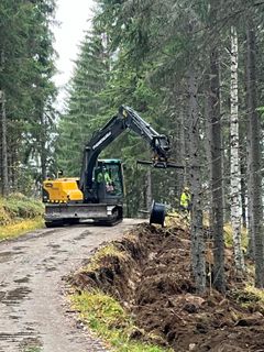 Kaivinkone kaivaa ojaa metsässä metsätien viereen.